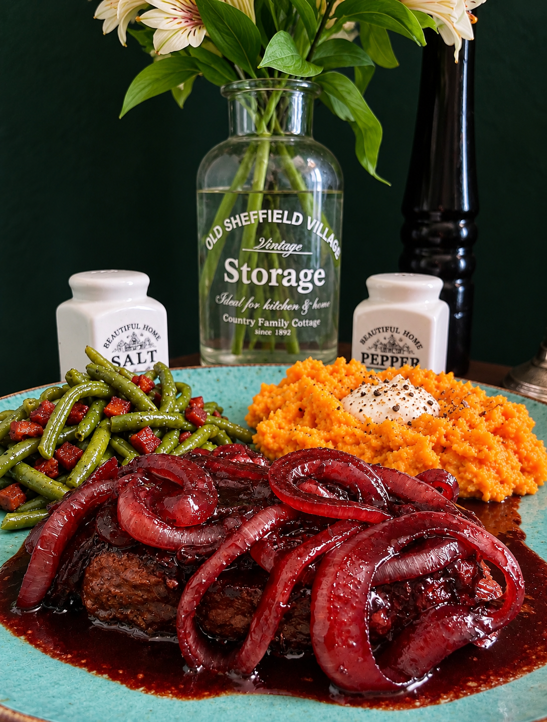 New Zealand-inspired plant-based steaks topped with glossy beetroot-glazed red onion rings, served with bright orange kūmara mash, vegan crème fraîche and green beans with crispy vegan bacon on a turquoise ceramic plate.